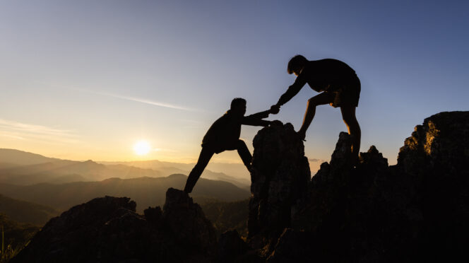 Silhouette Teamwork, Male hikers climbing up mountain cliff and one of them giving helping hand. People helping and, team work concept.