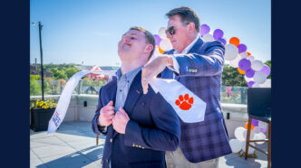 A young man beams proudly as Ward Carson puts his graduation stole over his shoulders