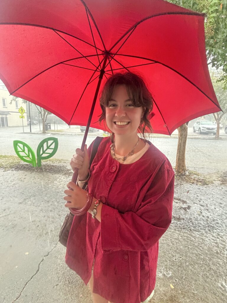 Savannah Hall stands holding a red umbrella