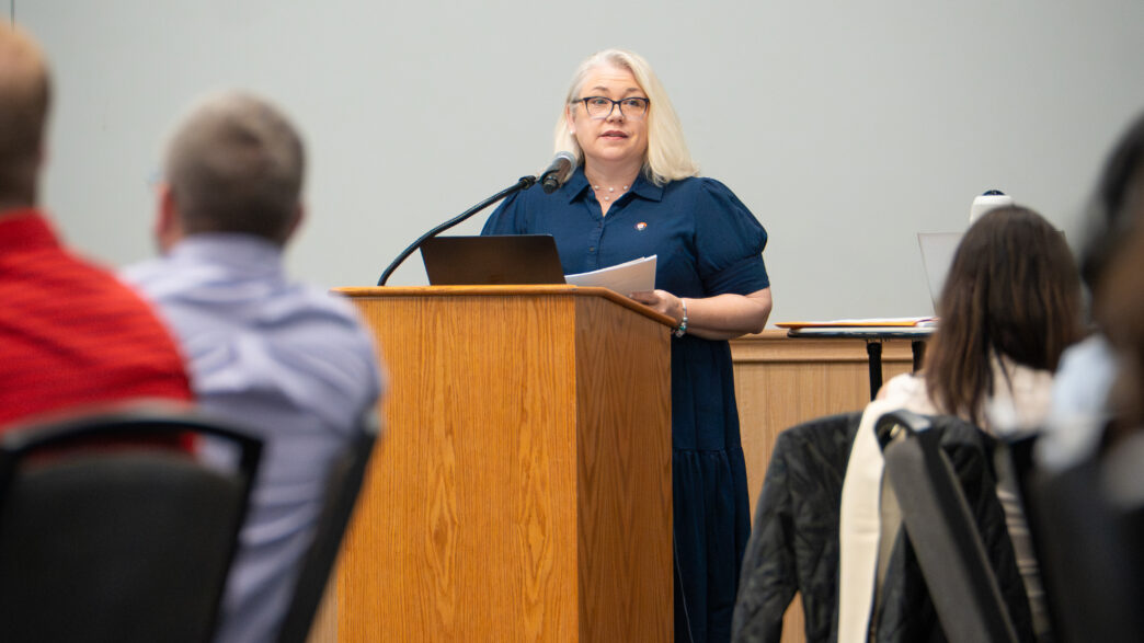 Kathy Bush Hobgood stands at a podium addressing a group of individuals
