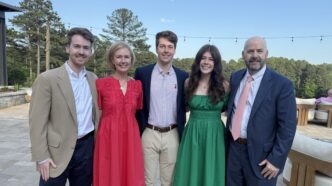 A family of five is dressed up and standing together as a group, three men and two women.