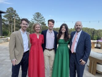 A family of five is dressed up and standing together as a group, three men and two women.