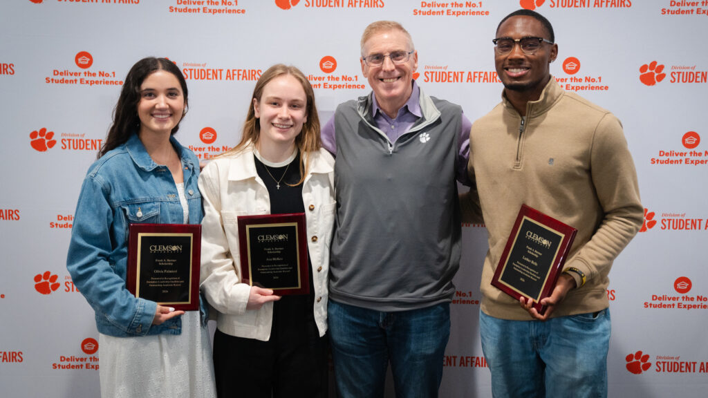 Three students hold award plaques alongside Doug Hallenbeck, vice president for student affairs