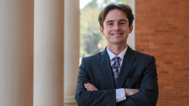 Owen Eastman stands in front of Sikes Hall in a suit with his arms crossed in front of him.