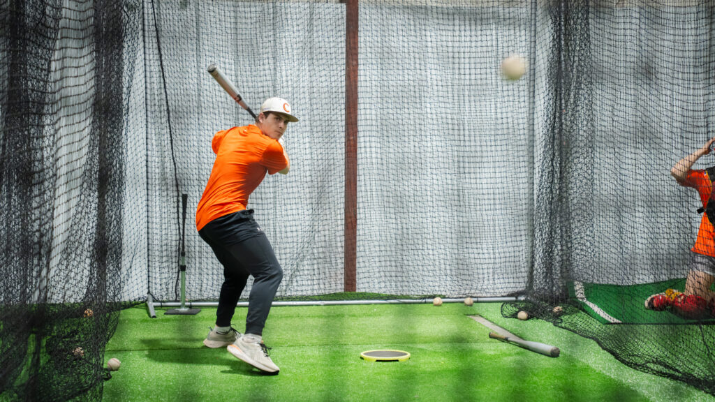 A male holding a baseball bat takes a swing in a batting cage