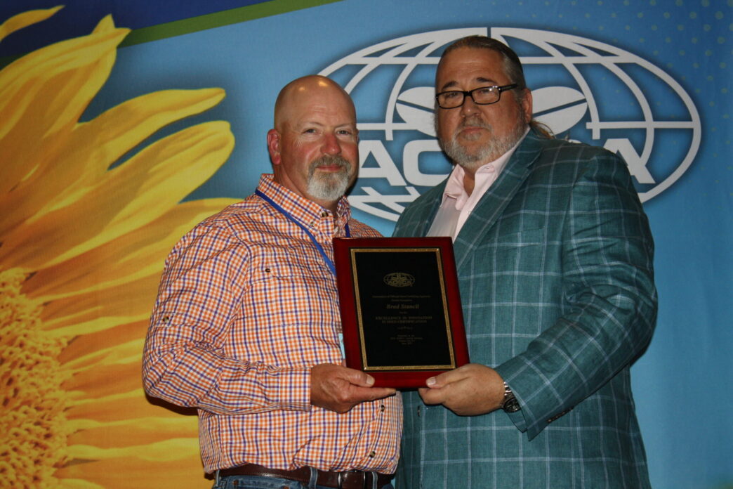 Brad Stancil stands on the left smiling as he receives an awards plaque from AOSCA president Billy Skaggs.
