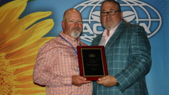 Brad Stancil stands on the left smiling as he receives an awards plaque from AOSCA president Billy Skaggs.