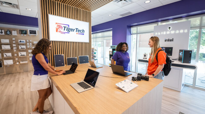 Customers browse laptops sitting on a wooden display in the Tiger Tech Shop.