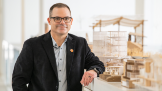 The Director of Facilities Enterprise for the Defense Health Agency Christopher Kiss, leans on a architecture project display case and looks into the camera. Kiss oversees the full life cycle of military health facilities.