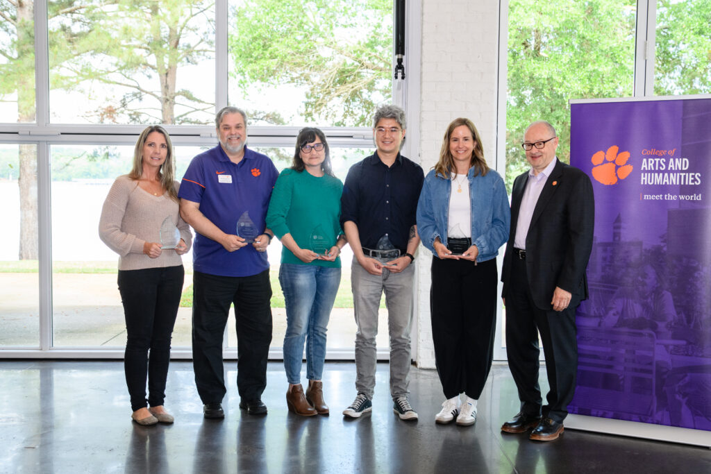 A group of College of Arts and Humanities faculty and staff smile for a photo holding awards.