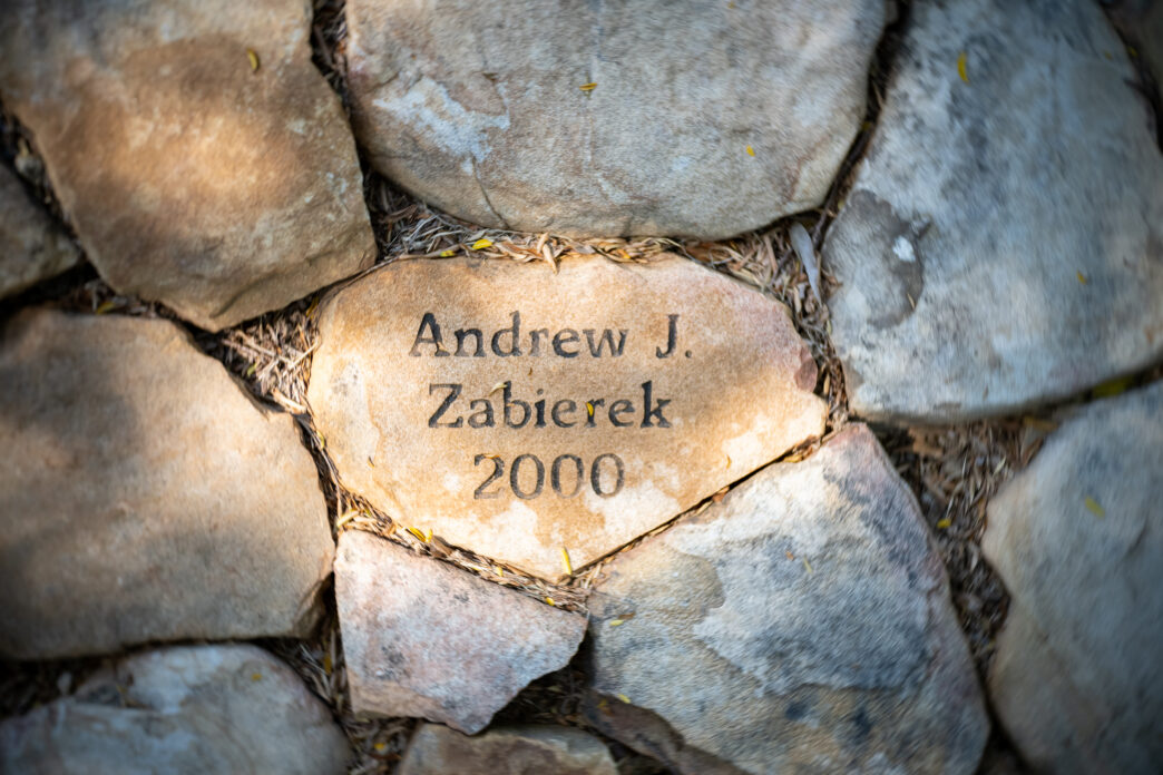 A flat stone with the name "Andrew J Zabierek 2000" etched into it in black letters lies among other stones