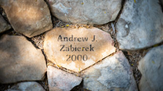 A flat stone with the name "Andrew J Zabierek 2000" etched into it in black letters lies among other stones