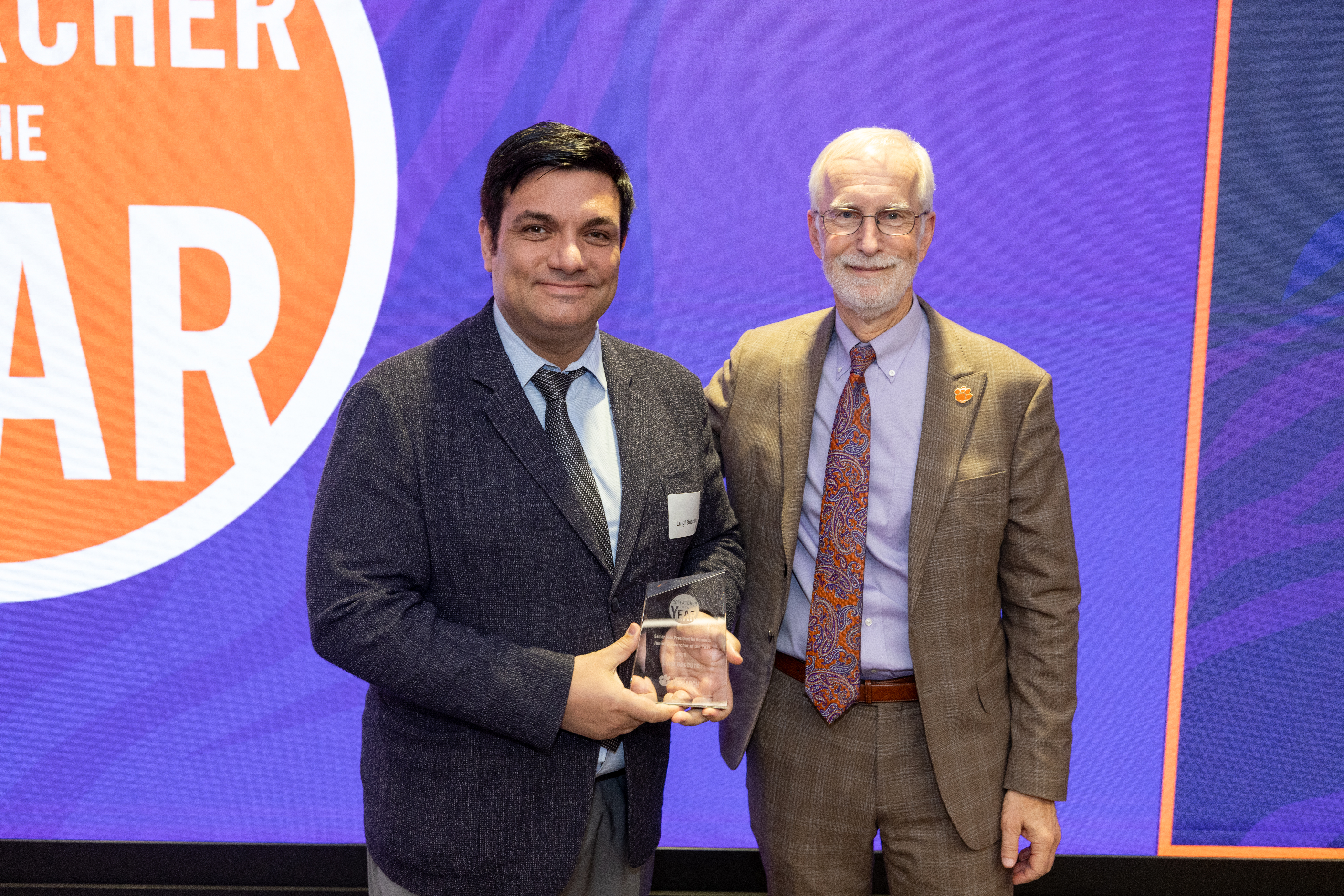 Two men pose for a photo with an award plaque