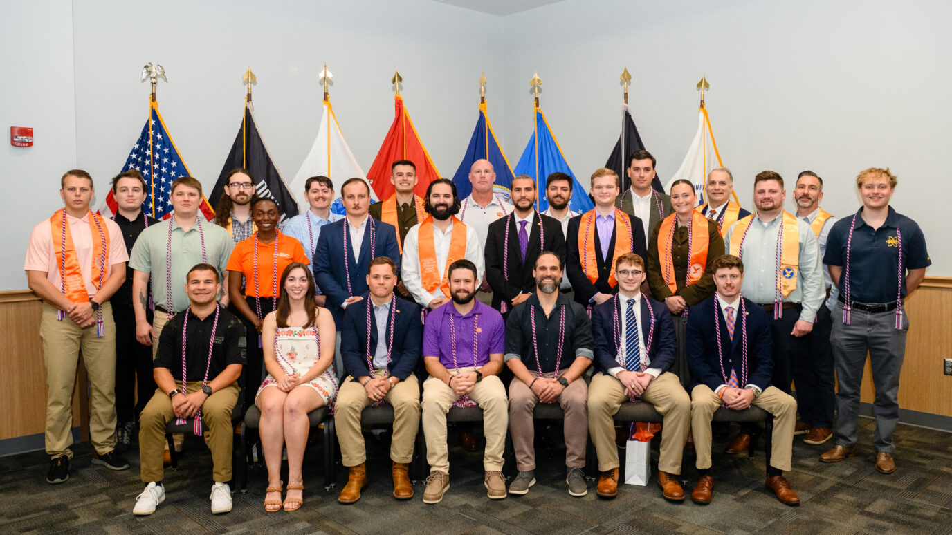 Individuals with red, white and blue cords and honor stoles in front of military flags