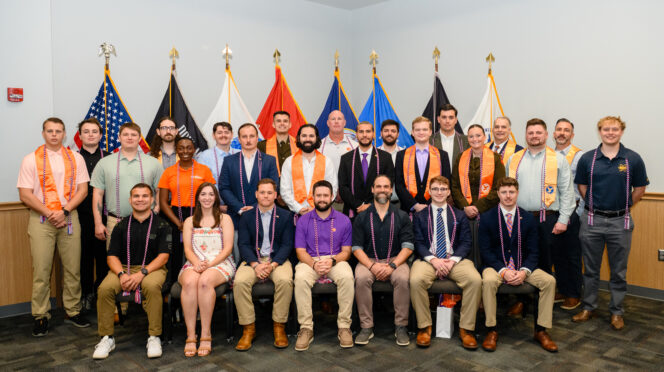 Individuals with red, white and blue cords and honor stoles in front of military flags