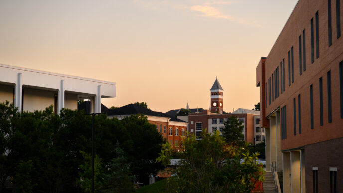 A panoramic view of sunrise on Clemson's campus, showing a library in the foreground and the tip of a bell tower in the background.