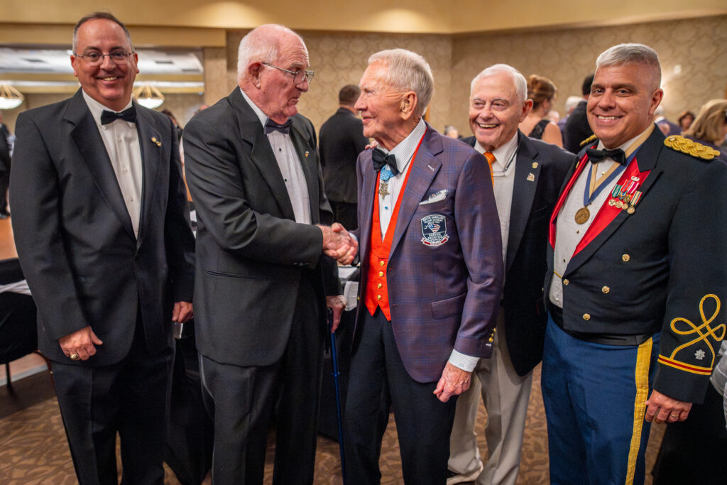 Five men in suits stand next to each other smiling and shaking hands