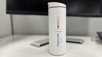 A white cylindrical water bottle with Clemson and Workday logos sits on a desk in front of a computer.