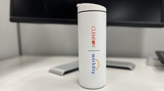 A white cylindrical water bottle with Clemson and Workday logos sits on a desk in front of a computer.