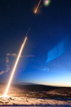A photo that shows a rocket with the light coming from the back to the ground, a cloud and a blue light in the sky.