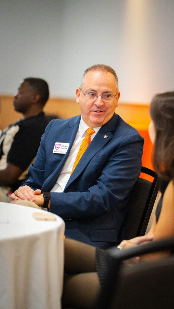 A man in a suit and tie speaks to a woman at a table