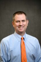 headshot of Stephen Kaeppler, a man with a short crew cut haircut wearing a blue shirt with orange tie.