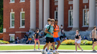 students walking on front of a bid, columned brick building