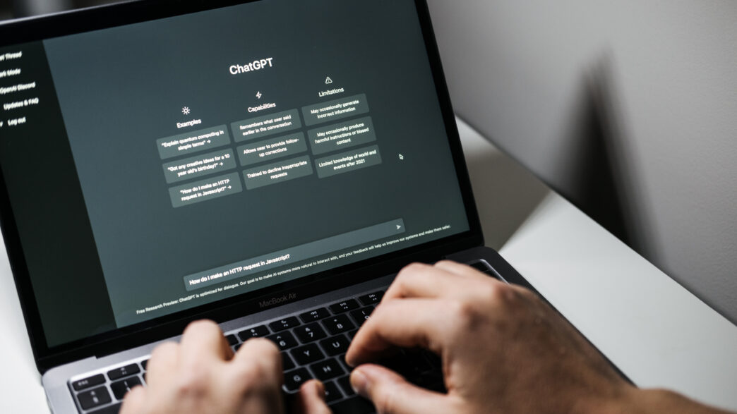 Hands type a prompt on a laptop into a ChatGPT text box.