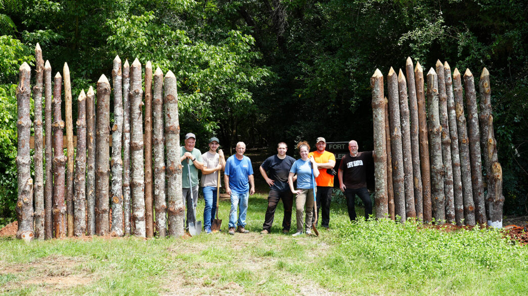 Clemson faculty and staff smile between walls of a partial recreation of Fort Rutledge, an important site in the American Revolution.