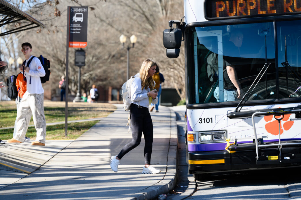 A female student wearing a bookbag steps onto a bus