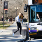 A female student wearing a bookbag steps onto a bus