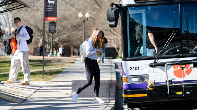 A female student wearing a bookbag steps onto a bus