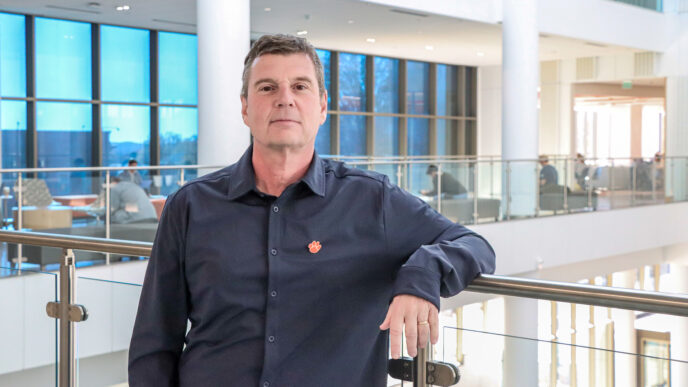 Scott Baier, Associate Dean of Research, for the Wilbur O. and Ann Powers College of Business at Clemson University. Scott is a white man with brown hair standing in the atrium of the Powers building. He is wearing a black button up shirt with an orange tiger paw on the right side of his body.