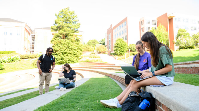 Students sit on the terraces of the amphitheater while using their laptops.