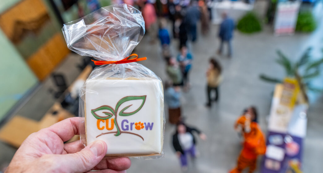 A hand holds a cookie with the CU Grow logo on it