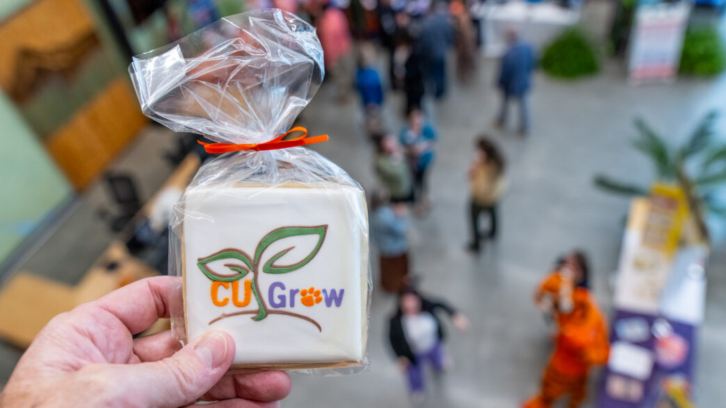 A hand holds a cookie with the CU Grow logo on it