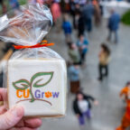 A hand holds a cookie with the CU Grow logo on it