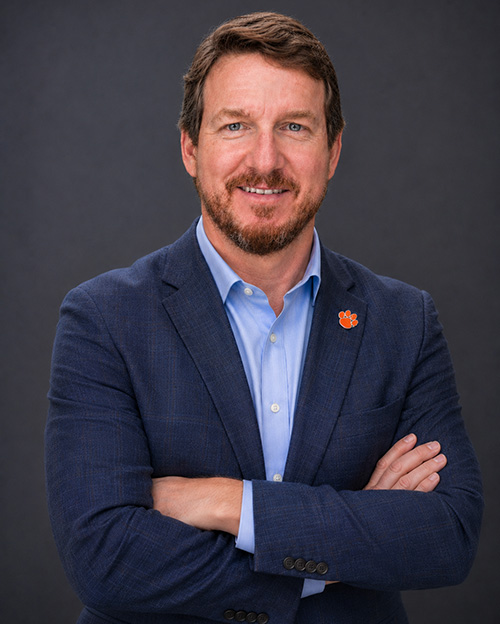 A man in a navy blazer with a Clemson tiger paw lapel pin.