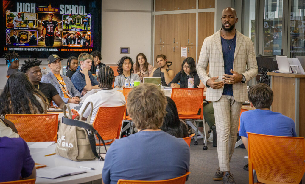A man in a tan suit walks through a classroom full of students