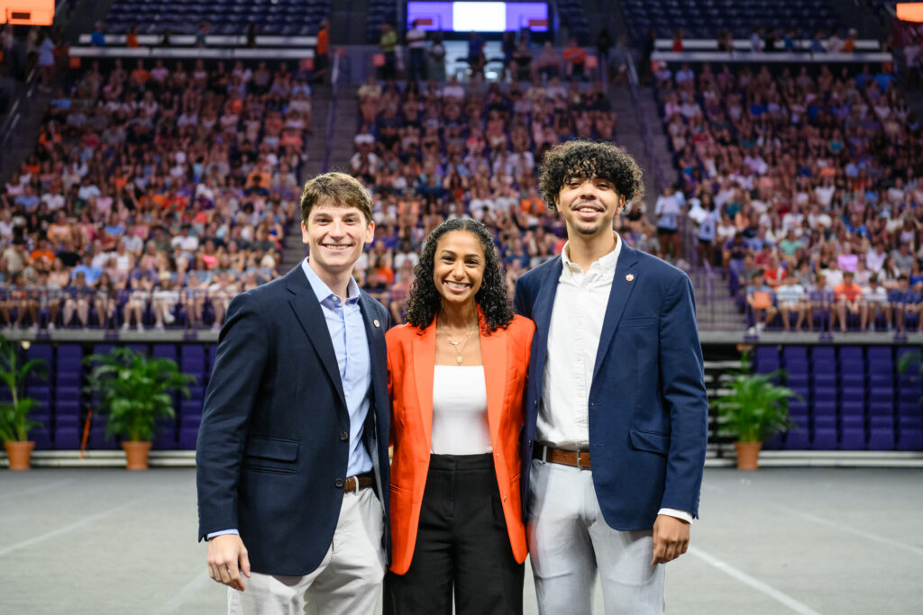 Three people in business attire pose for a photo with a crowd in the background