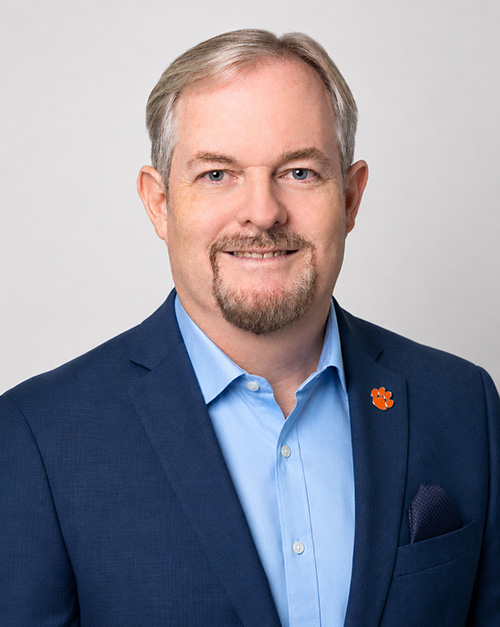 A man in a navy blazer with a Clemson Tiger Paw lapel pin.