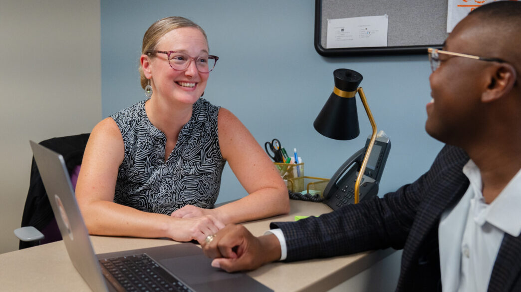 Megan Fallon talks with a student at a desk in an office on campus
