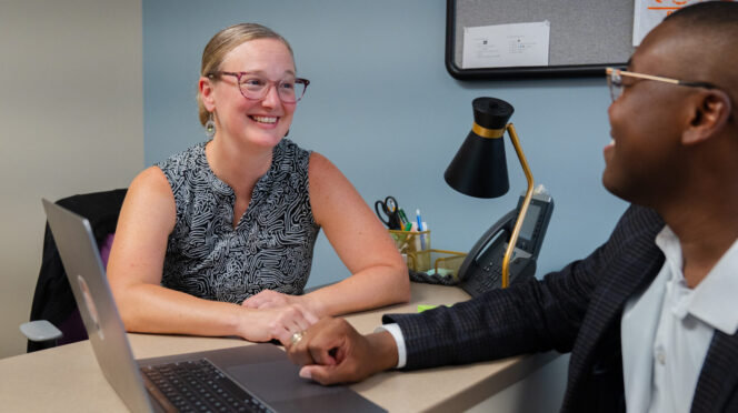 Megan Fallon talks with a student at a desk in an office on campus