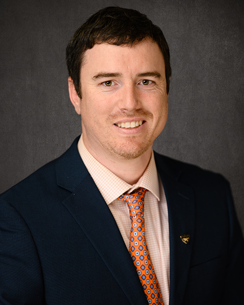 A man in a dark suit with an orange tie