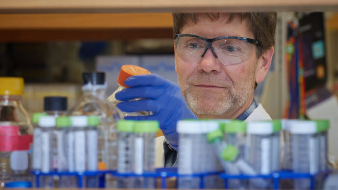 A man wearing glasses picks up a bottle in a science lab