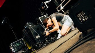 Clemson alum Sophie Ayers crouched down on a concert stage, taking a photo of the band Winyah while they perform.