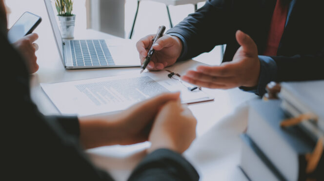 Two people's hands leaning on a desk. One person's hands are open and holding a pen, as if explaining while speaking.