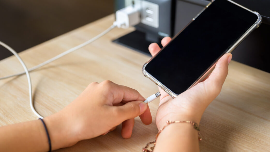 Closeup hand going to charge mobile phone battery from the built-in power socket on the table.