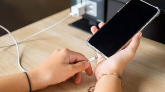 Closeup hand going to charge mobile phone battery from the built-in power socket on the table.