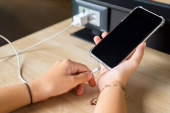 Closeup hand going to charge mobile phone battery from the built-in power socket on the table.